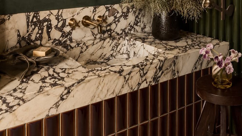 A veined marble basin with brass taps on a fluted brown tile base.