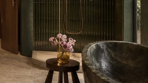A green stone bath beside a small wooden stool with orchids.
