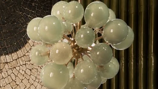 A pale green glass globe pendant against fluted green tiles.