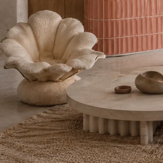 A cream shell-shaped armchair beside a round stone coffee table on a jute rug.
