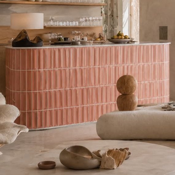 A curved bar in glazed pink tile below open oak shelves and a patterned stone wall.