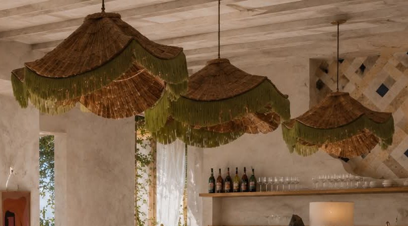 Three woven rattan pendants with green fringing hanging from a beamed ceiling.