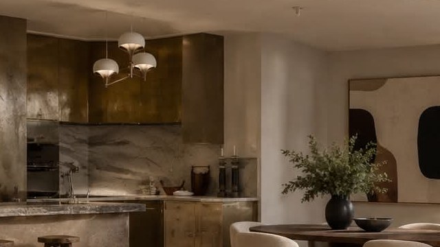 A kitchen in antiqued brass with a veined marble splashback and turned wood stools.