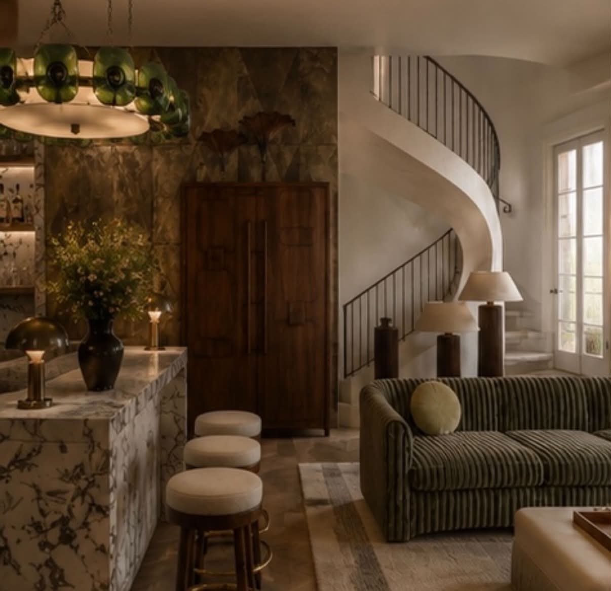 A marble bar with stools beside a green fluted sofa and a curved stone staircase.