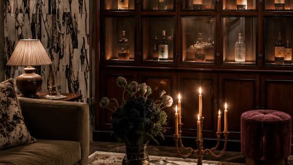A glazed walnut bar cabinet beside a marble wall, with candles on a marble table.