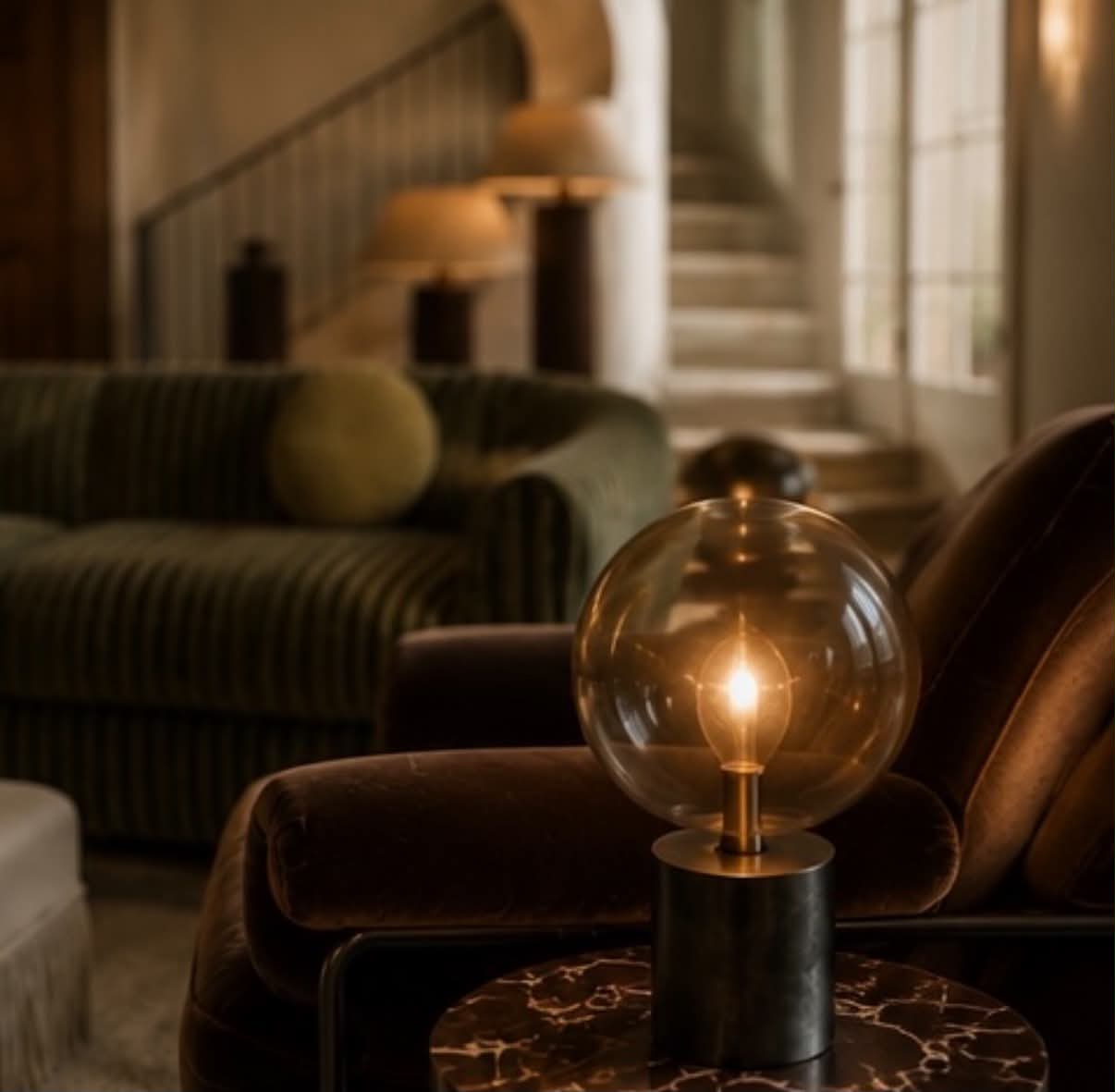A lit glass globe lamp on a marble side table beside a stone staircase.