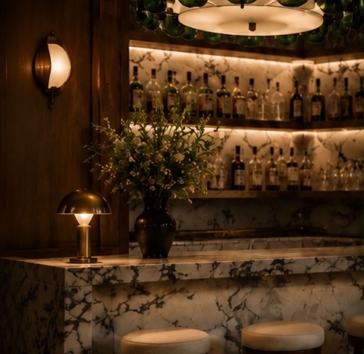 A marble bar with brass lamp, green glass pendant and backlit shelving.