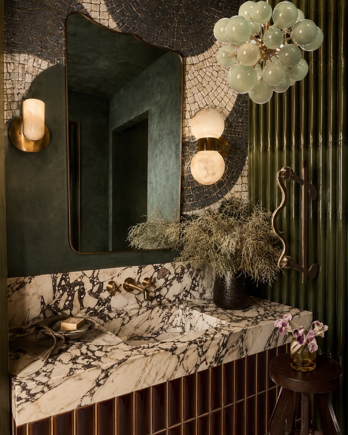 A green cloakroom with mosaic walls, veined marble basin and alabaster sconces.